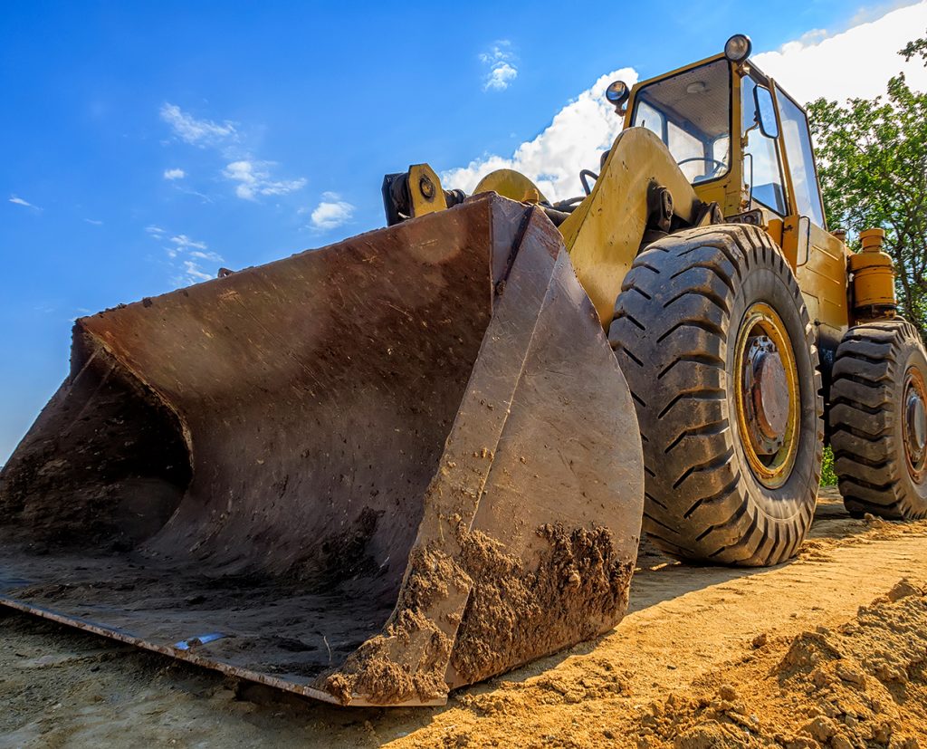 Yellow construction bulldozer with a large bucket on sandy ground under a clear blue sky.