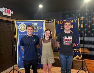 Three students stand in front of Rotary Banners.